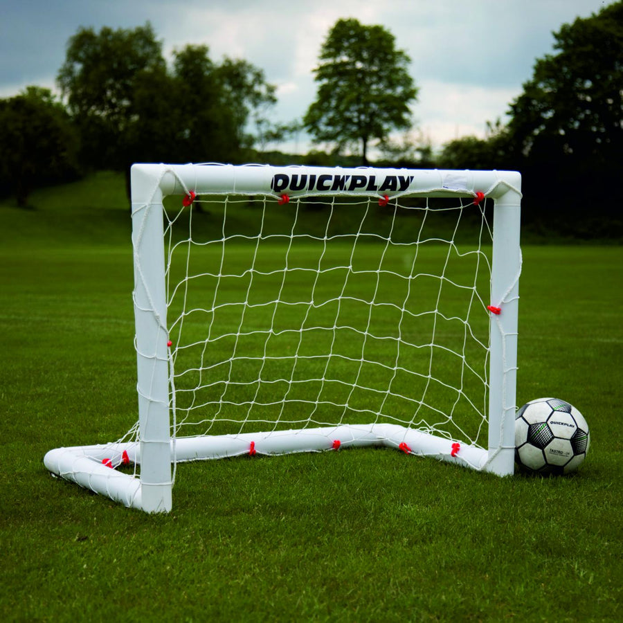 Mini-but de football Q-FOLD 90 x 75 cm avec cadre et filet blancs sur l'herbe, un ballon de football à côté.