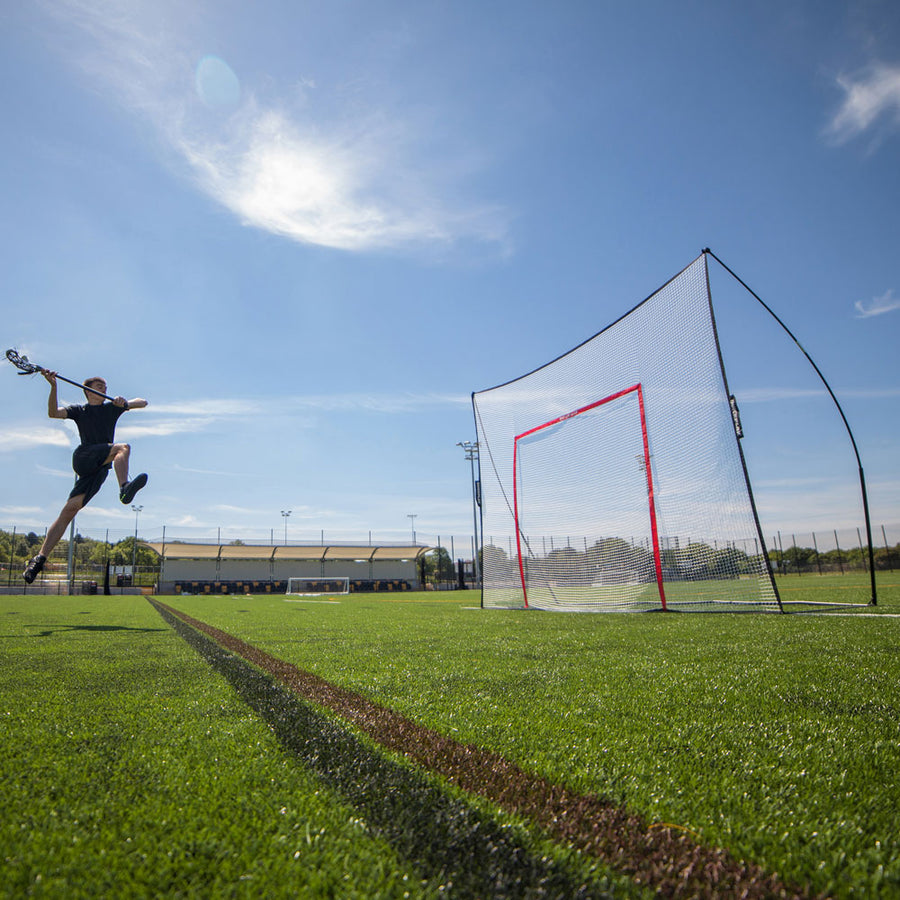 Joueur de lacrosse sautant pour tirer sur une section de MEGA NET munie d'un cadre cible orange, sur un terrain synthétique.