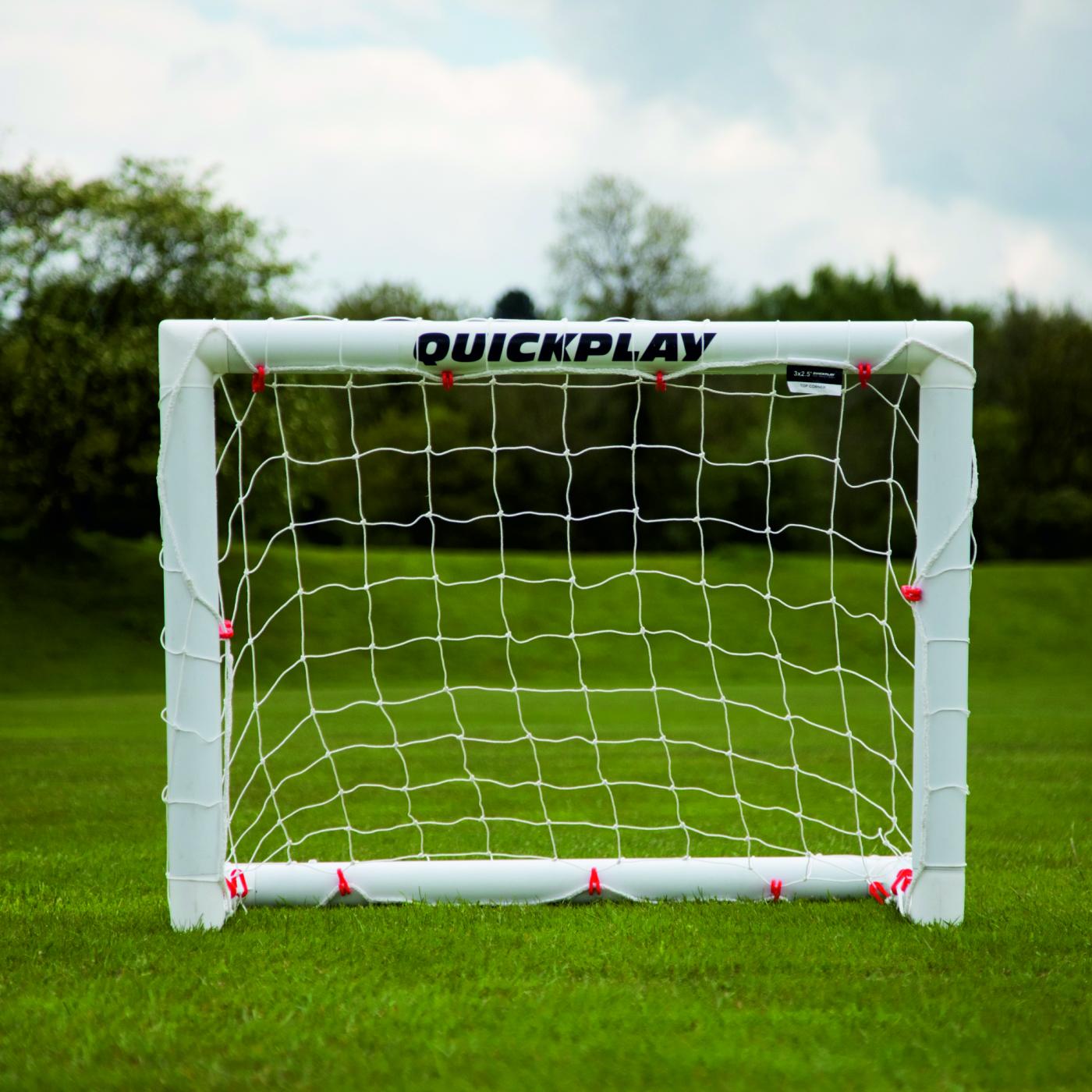 Mini-but de football Q-FOLD 90 x 75 cm vu de face sur l'herbe, avec QUICKPLAY sur la barre transversale blanche.