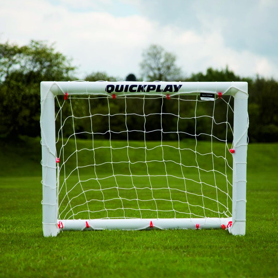 Mini-but de football Q-FOLD 90 x 75 cm vu de face sur l'herbe, avec QUICKPLAY sur la barre transversale blanche.