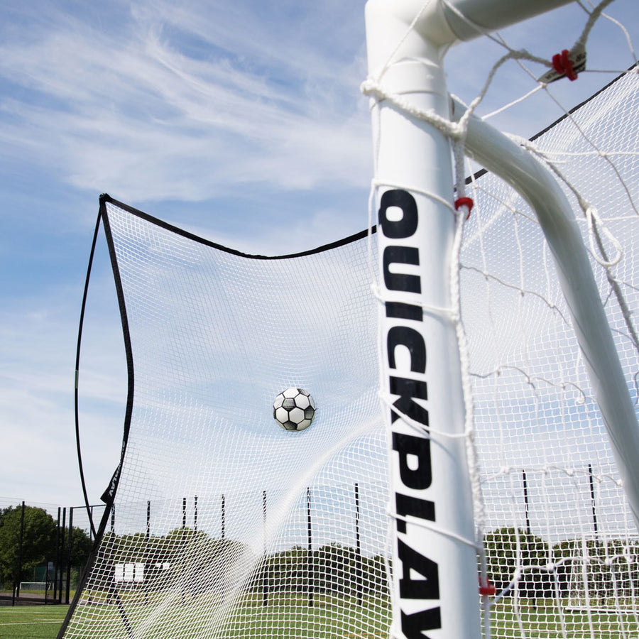 MEGA NET XL arrêtant un ballon de football derrière un but, avec un poteau de but QUICKPLAY blanc au premier plan.