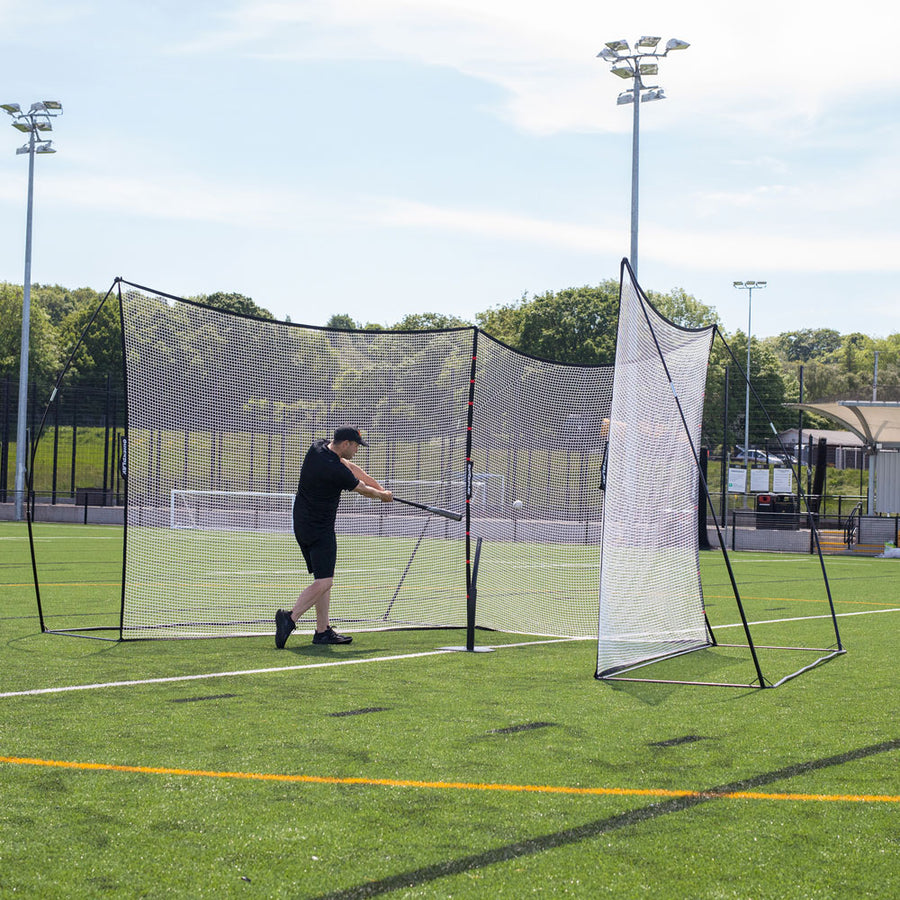 Homme balançant une batte de baseball à l'intérieur du MEGA NET XL, installé avec des sections latérales inclinées sur un terrain synthétique.