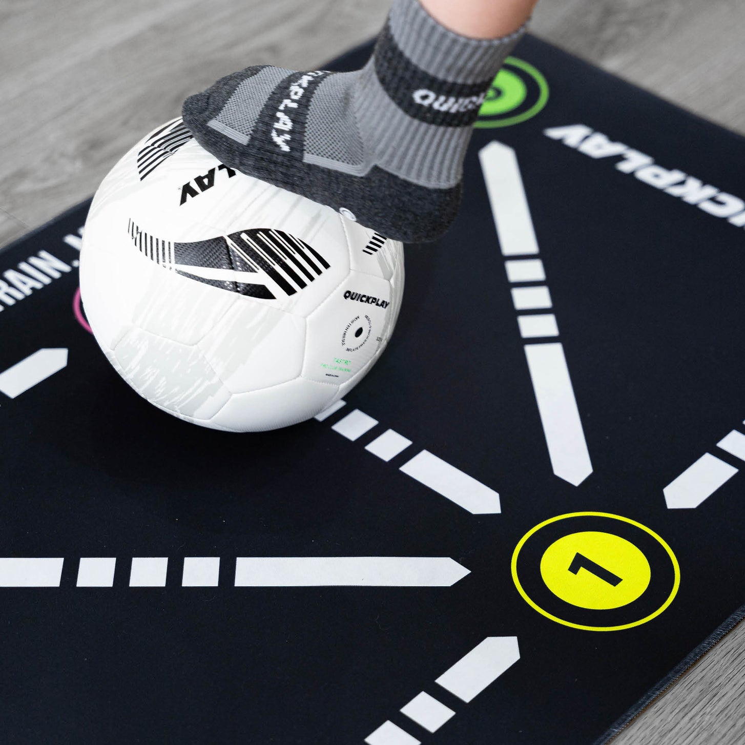 Gros plan du tapis d'entraînement de football pour la maîtrise du ballon, pied en chaussette grip QUICKPLAY sur un ballon blanc à côté du chiffre 1 jaune.