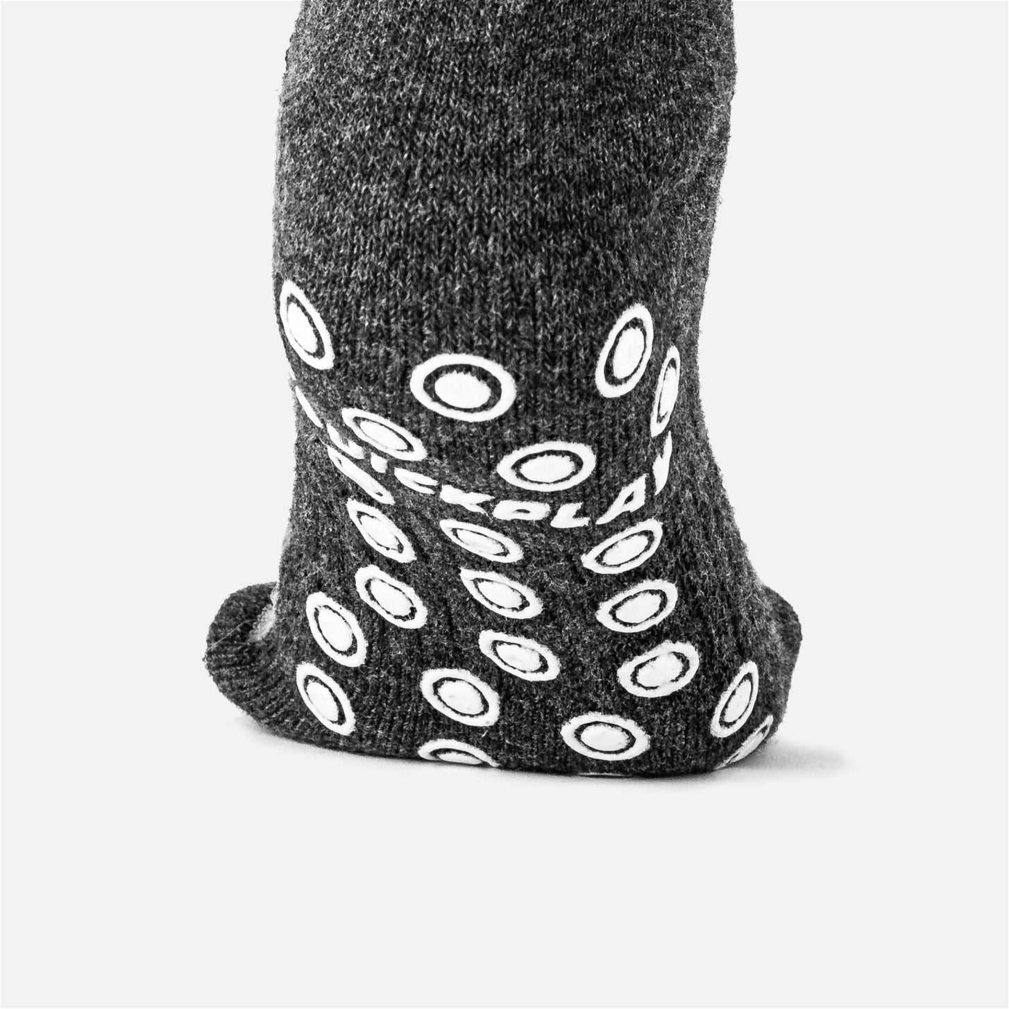 Gros plan de la semelle d'une chaussette grip QUICKPLAY gris foncé, montrant les pastilles antidérapantes blanches en forme d'anneau et le logo QUICKPLAY.