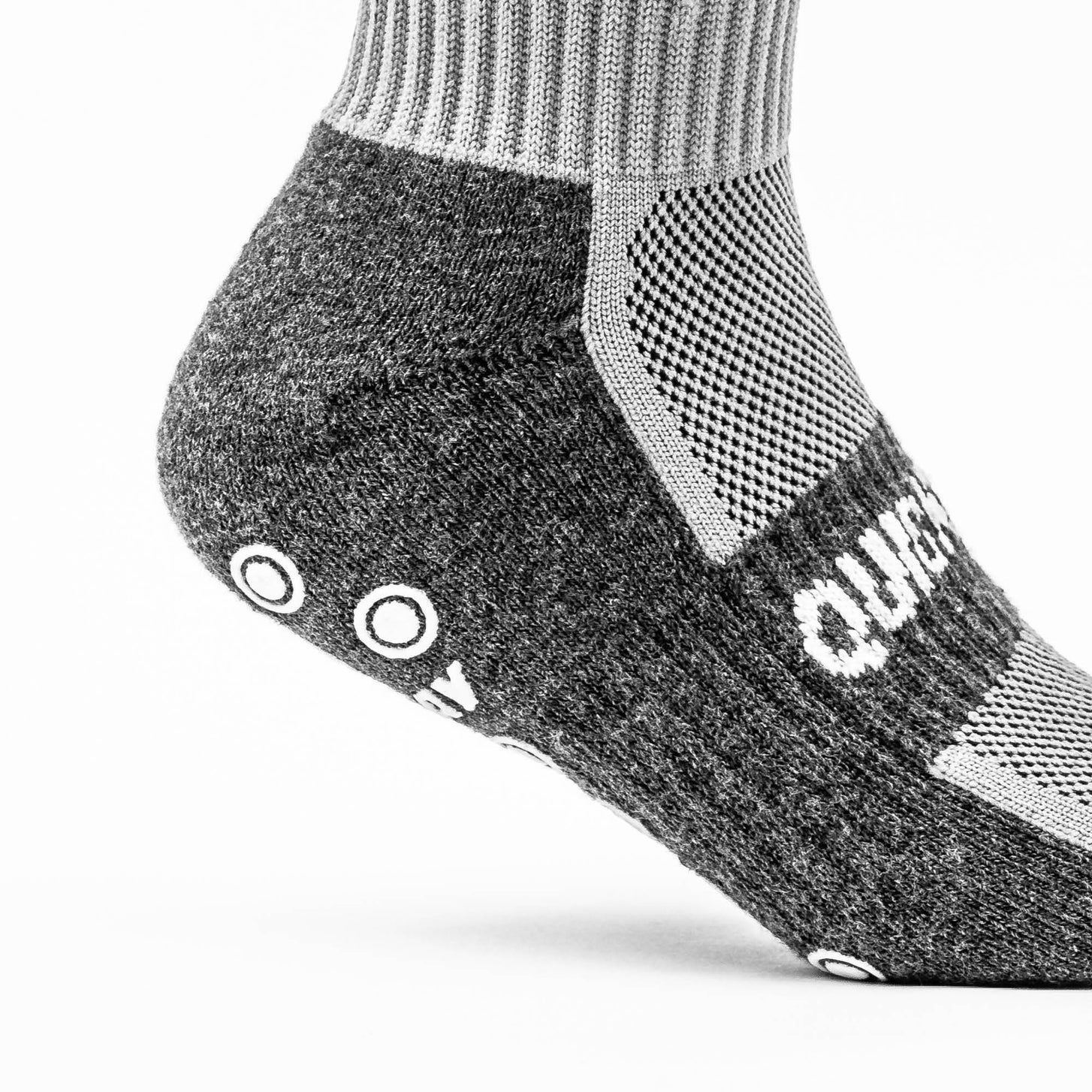 Gros plan du talon et de la cheville d'une chaussette grip QUICKPLAY, montrant le pied rembourré gris foncé et le panneau en maille ajourée gris clair.