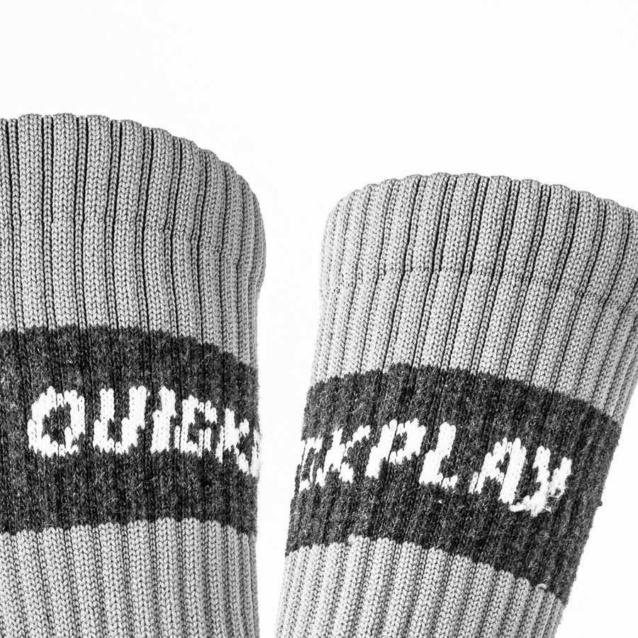 Gros plan des bords-côtes gris clair de deux chaussettes grip QUICKPLAY, avec la bande QUICKPLAY gris foncé.