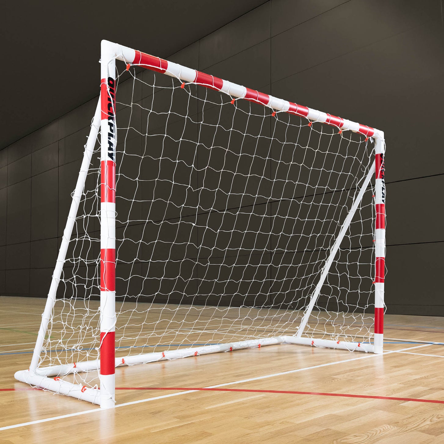 But de handball pliable Q-FOLD 300 x 200 cm avec des poteaux rayés rouge et blanc et un filet blanc, sur le parquet d'une salle de sport.