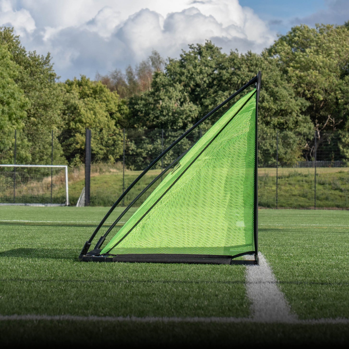 But KICKSTER PRO 150 x 100 cm vu de profil, montrant son filet vert incliné, sur un terrain synthétique avec des arbres derrière.