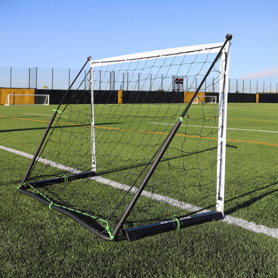 KICKSTER Elite 150 x 100 cm vu depuis un angle arrière sur un terrain synthétique, montrant le cadre noir et les attaches vertes.