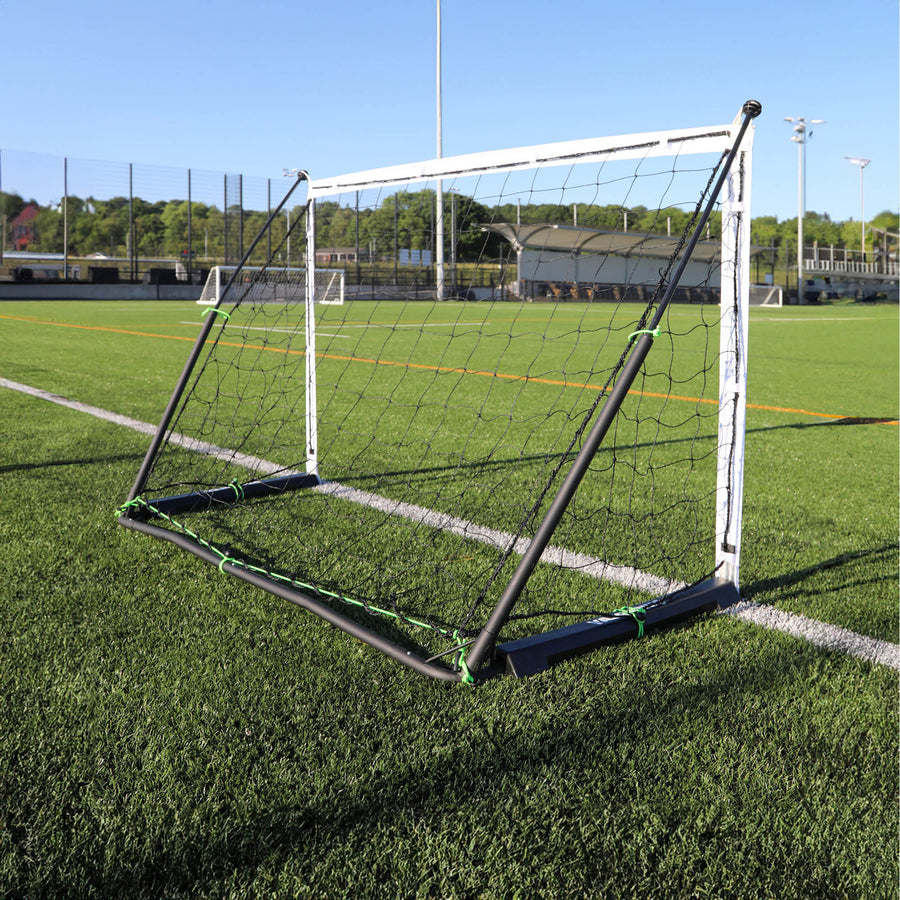 But KICKSTER Elite 180 x 120 cm vu de derrière sur un terrain synthétique, montrant le cadre arrière noir et les clips du filet.