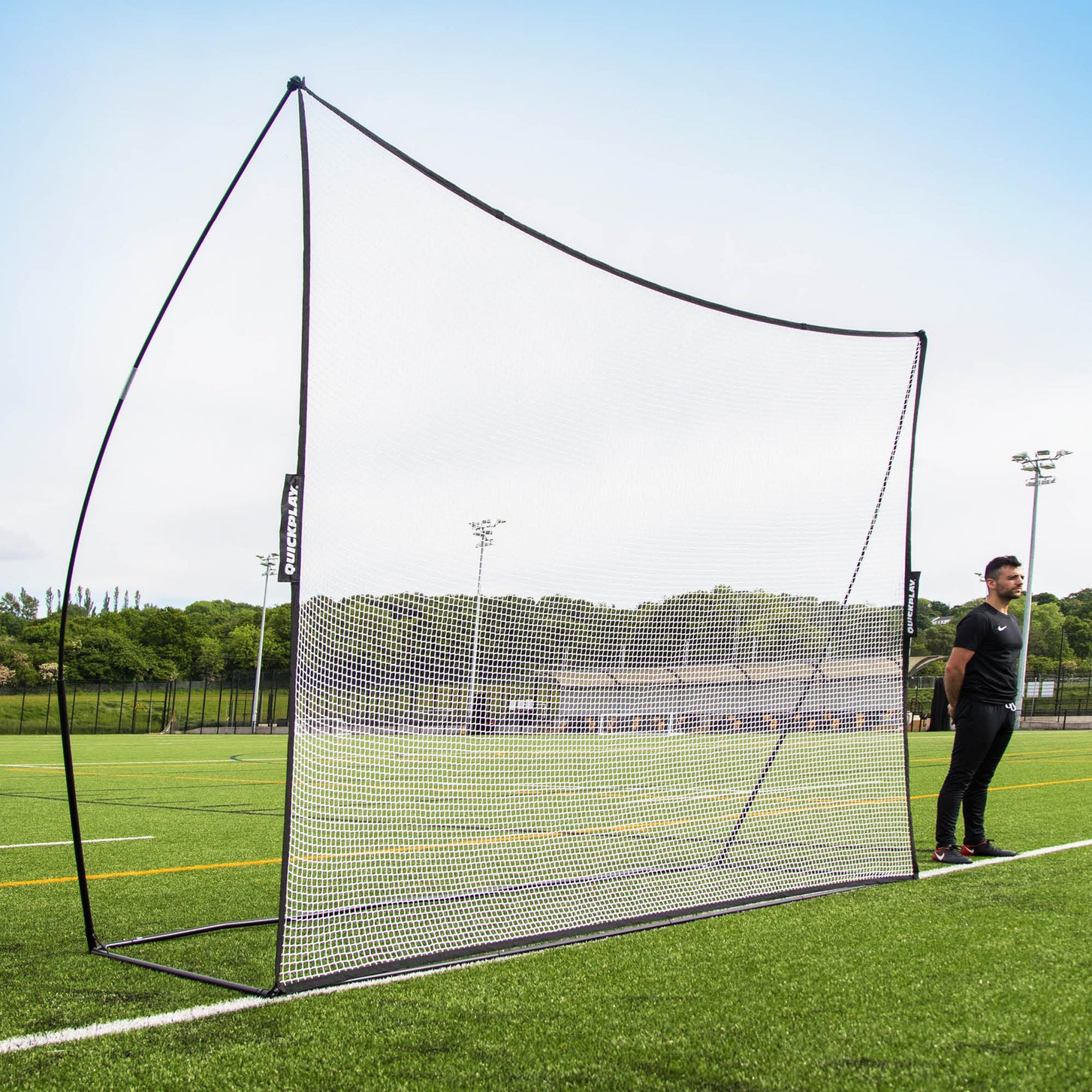 Filet pare-ballons MEGA NET 370 x 270 cm avec cadre noir et filet blanc sur un terrain synthétique, un homme debout à côté.