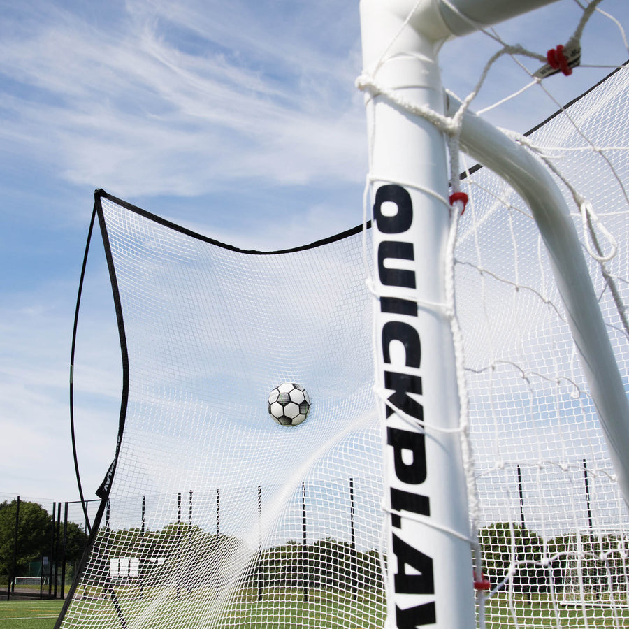 Filet pare-ballons MEGA NET 370 x 270 cm arrêtant un ballon de football derrière un poteau de but QUICKPLAY blanc, vu en contre-plongée.