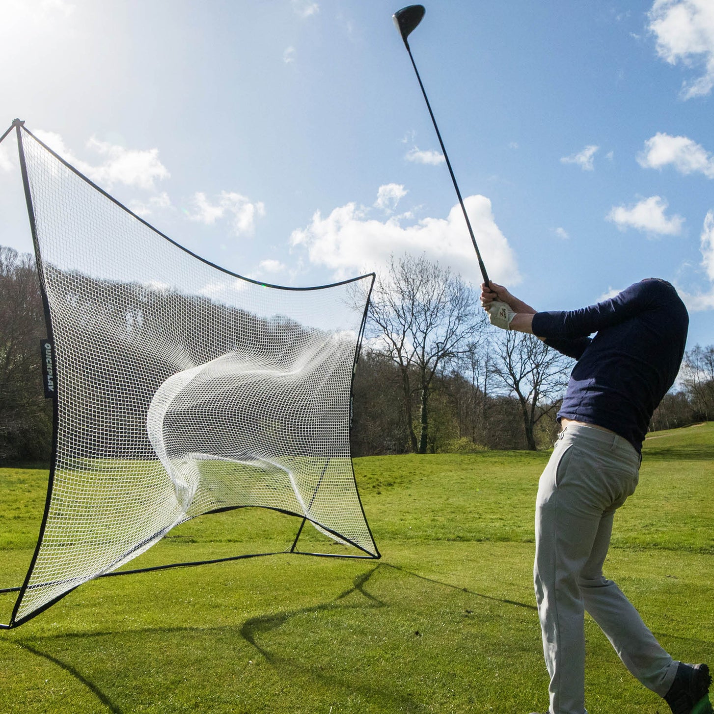 Filet pare-ballons MEGA NET 370 x 270 cm sur un terrain en herbe, un golfeur terminant son swing au driver après avoir envoyé une balle dans le filet.
