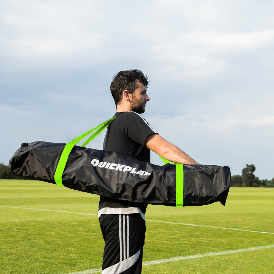 Homme portant le MEGA NET 370 x 270 cm dans son sac noir QUICKPLAY à sangles vertes sur un terrain en herbe.