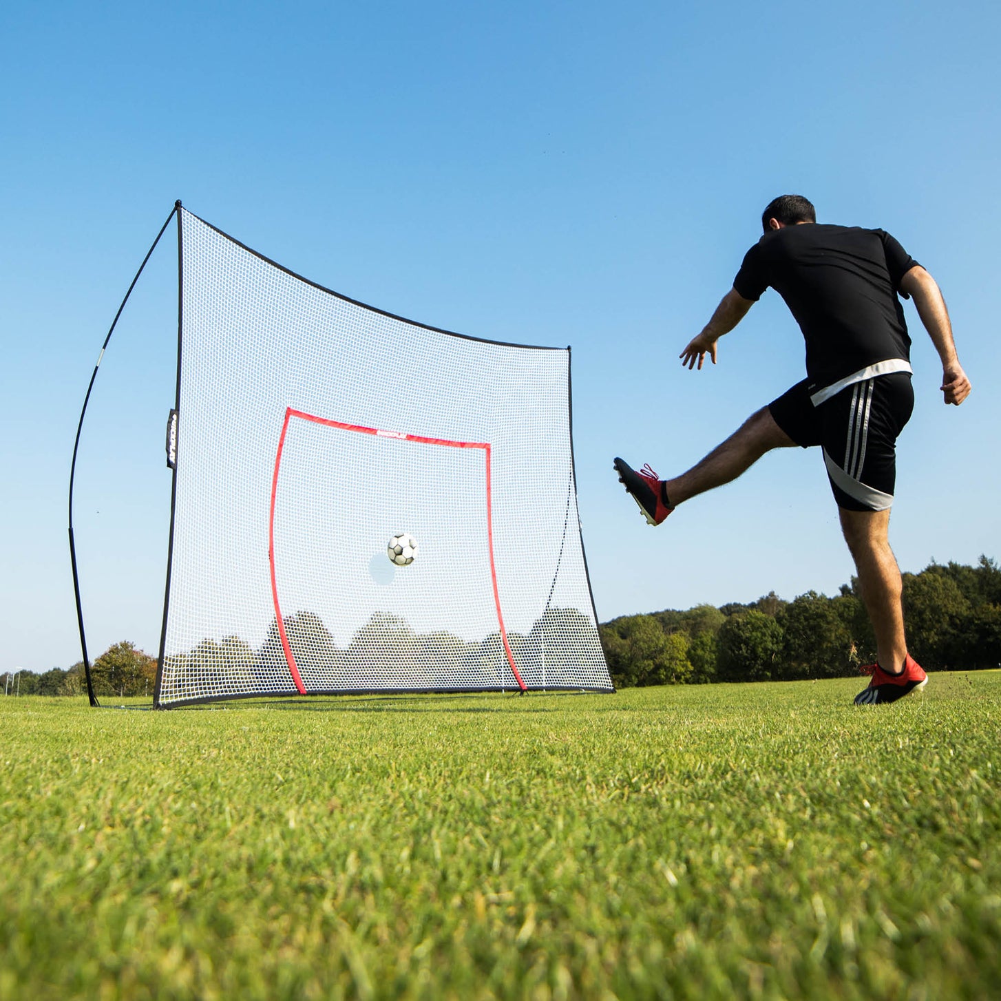 Joueur frappant un ballon dans le MEGA NET 370 x 270 cm sur l'herbe, le ballon filant vers le cadre cible orange.