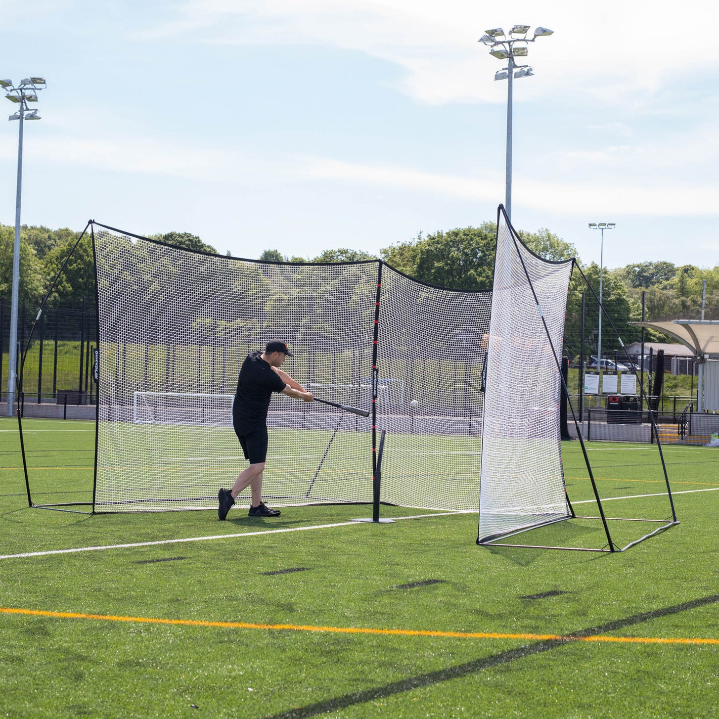 Filets pare-ballons MEGA NET 370 x 270 cm sur un terrain synthétique, un joueur frappant une balle de baseball avec une batte dans les filets.