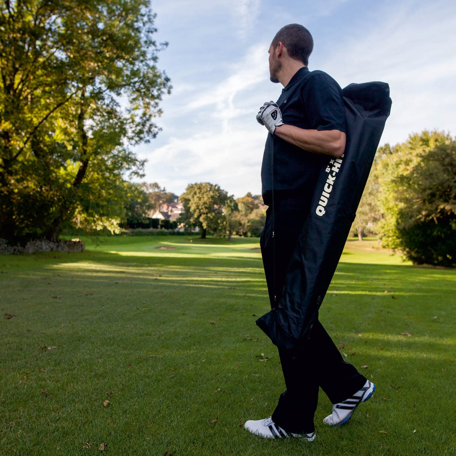 Golfeur portant sur l'épaule le filet de golf QUICK-HIT rangé dans son sac noir QUICK-HIT, sur un parcours de golf.