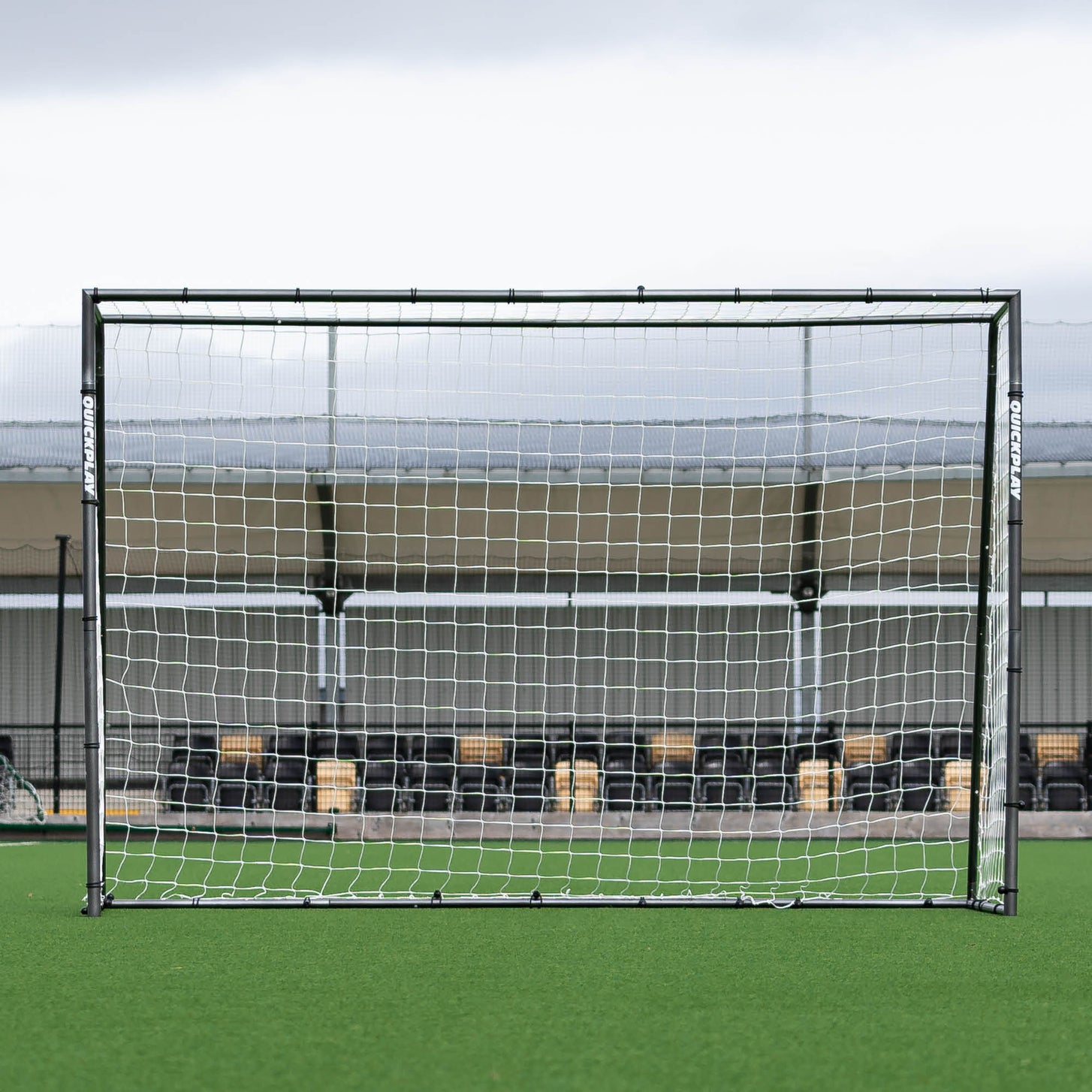 But de futsal GS Series 300 x 200 cm vu de face, devant une tribune au bord d'un terrain synthétique.