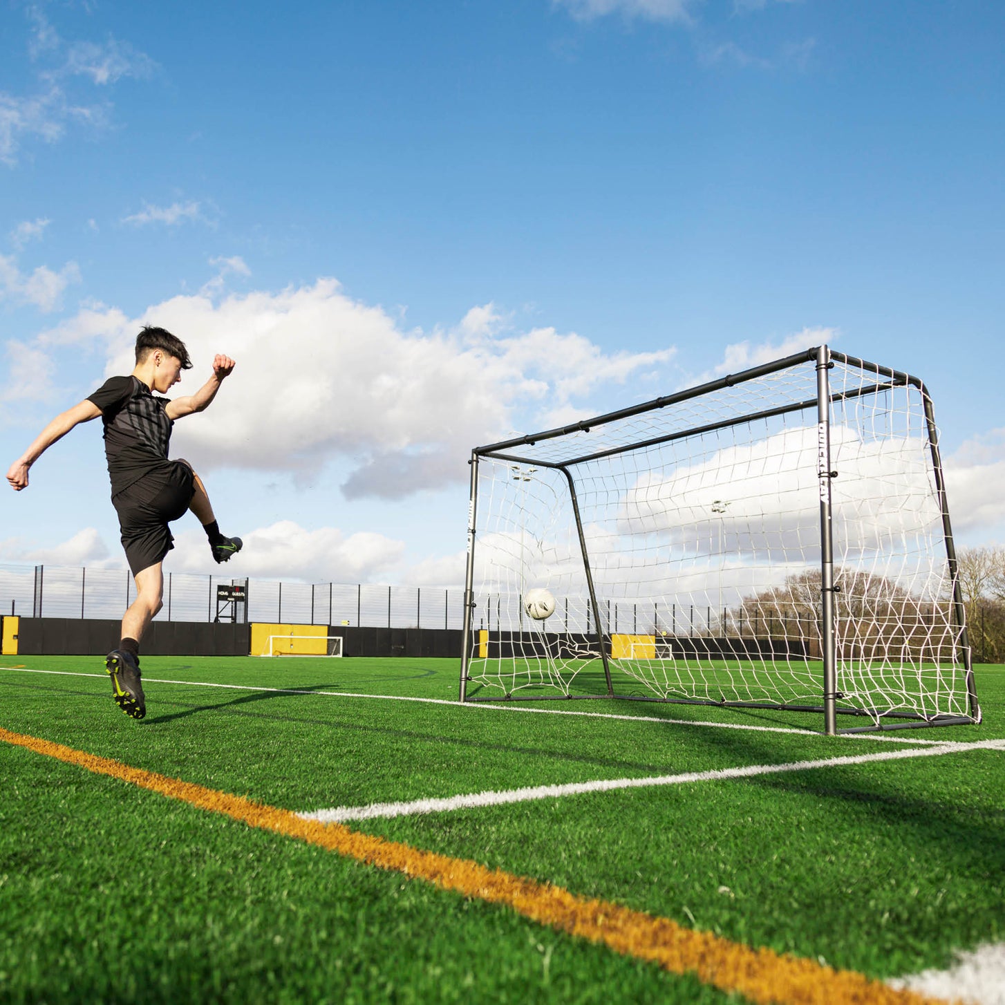 Joueur tirant sur le but de futsal GS Series 300 x 200 cm sur un terrain synthétique, le ballon filant dans le filet.