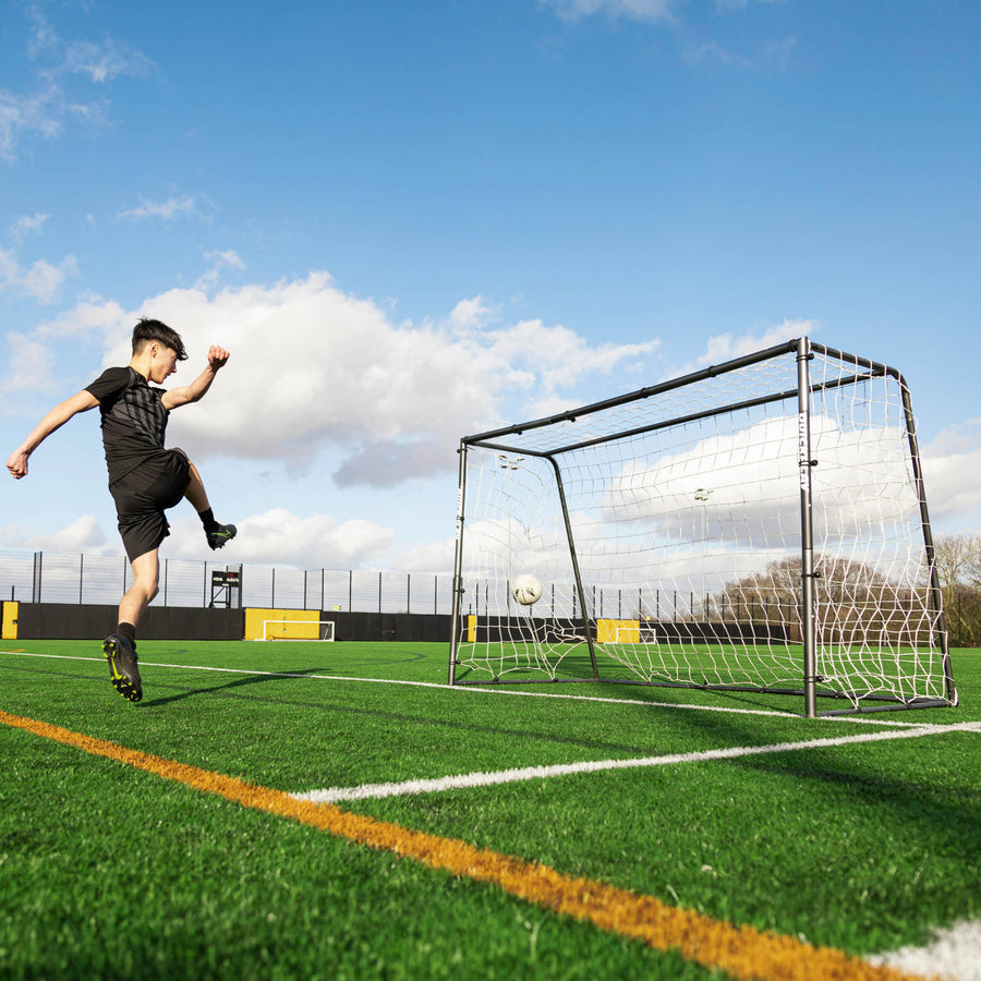 Joueur tirant sur le but de futsal GS Series 300 x 200 cm sur un terrain synthétique, le ballon filant dans le filet.