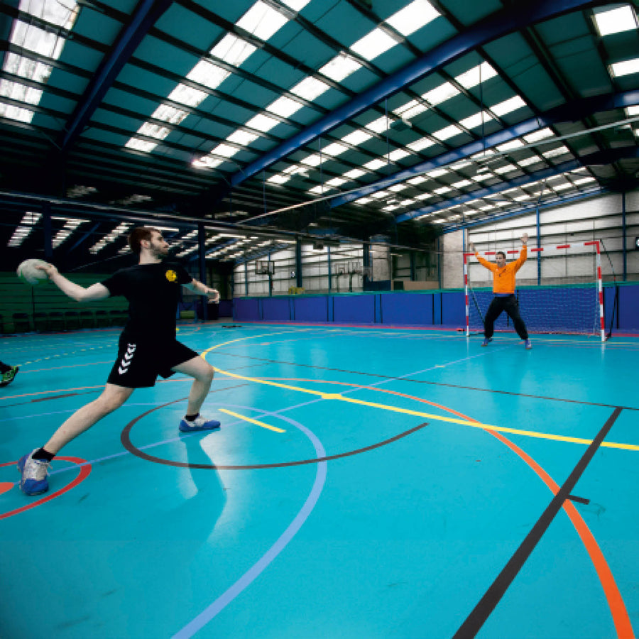 Joueur lançant un ballon de handball vers un gardien devant le but de minihand transportable 240 x 170 cm dans une grande salle.