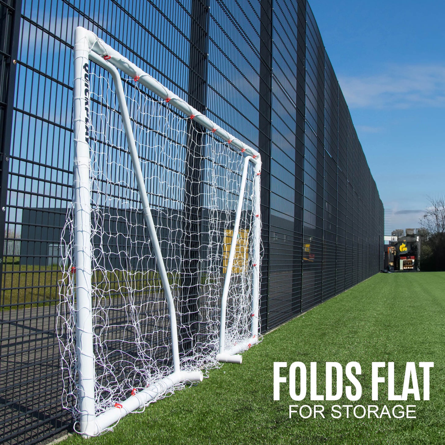 But Q-FOLD Match 300 x 200 cm plié à plat contre une clôture sur un terrain synthétique, avec le texte « Folds flat for storage ».