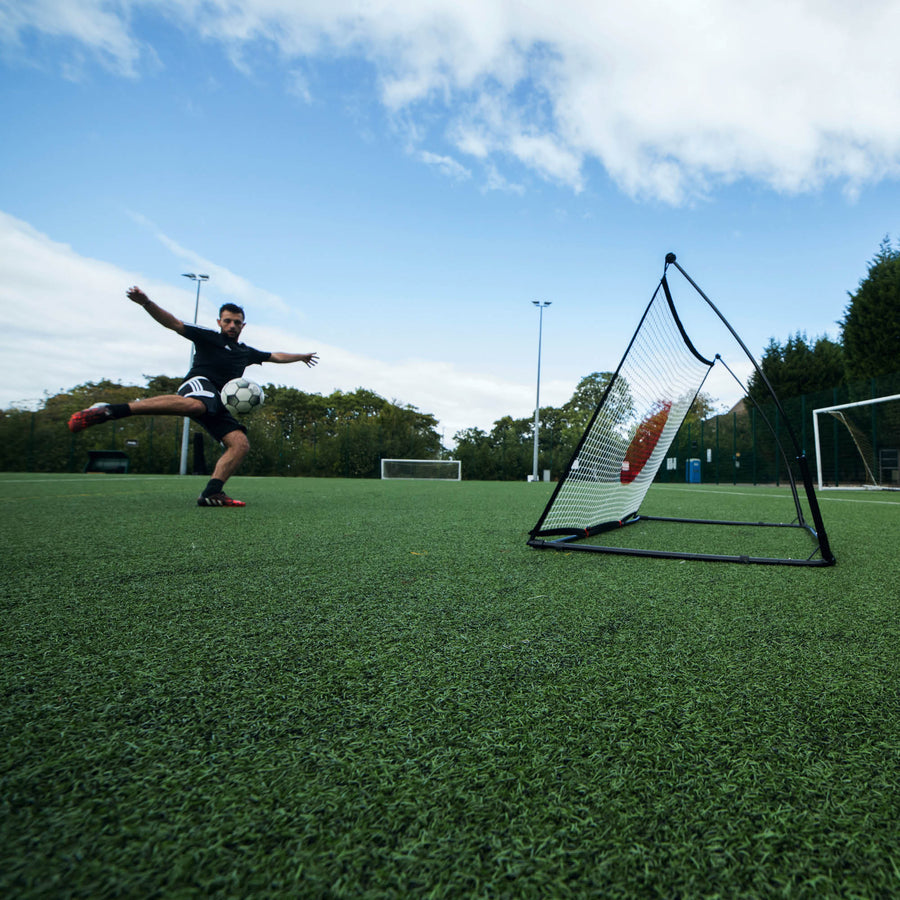 Joueur frappant de volée vers le rebondisseur de football SPOT 150 x 100 cm sur un terrain synthétique, vu en contre-plongée grand angle.