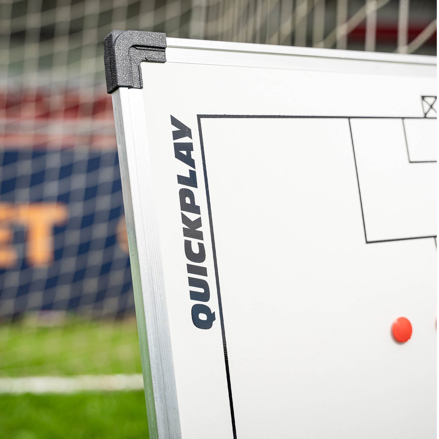 Gros plan d'un coin du tableau tactique de football magnétique 60 x 90 cm, montrant le cadre argenté, l'embout d'angle noir et le logo QUICKPLAY.