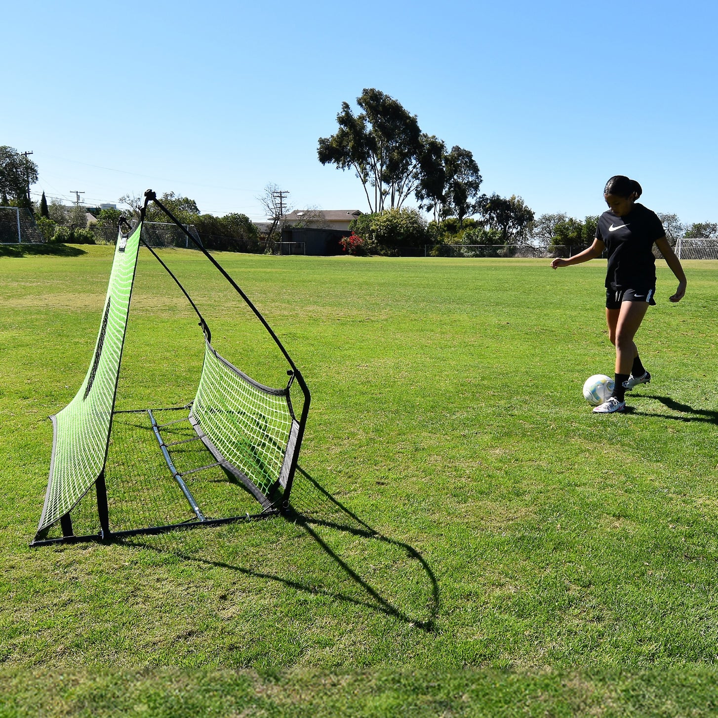 Joueur sur le point de passer un ballon dans le rebondisseur de football à double filet TEKKERS Trainer, vu de côté sur l'herbe.