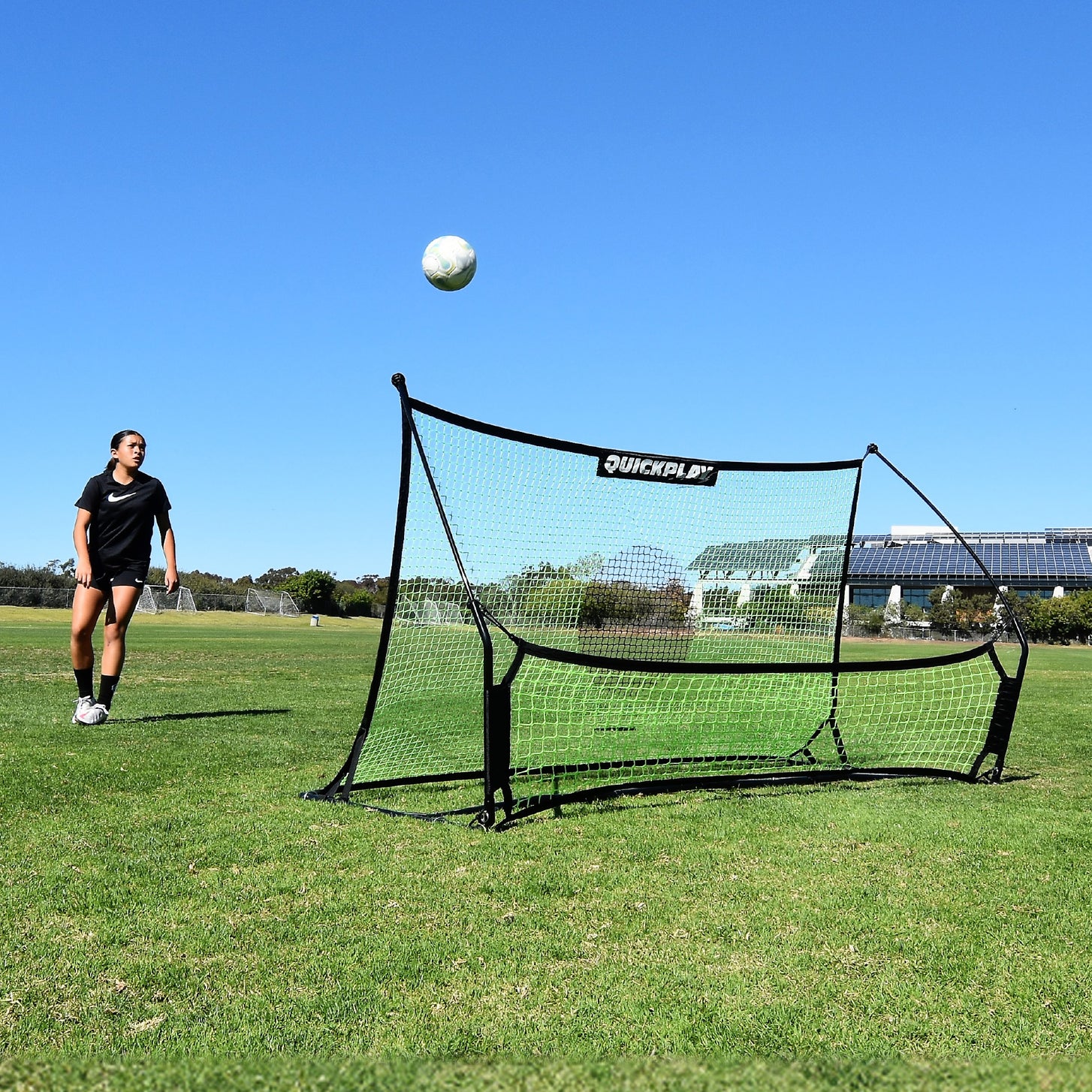 Joueur regardant un ballon s'élever depuis le filet du TEKKERS Trainer, vue de face du rebondisseur sur un terrain en herbe.