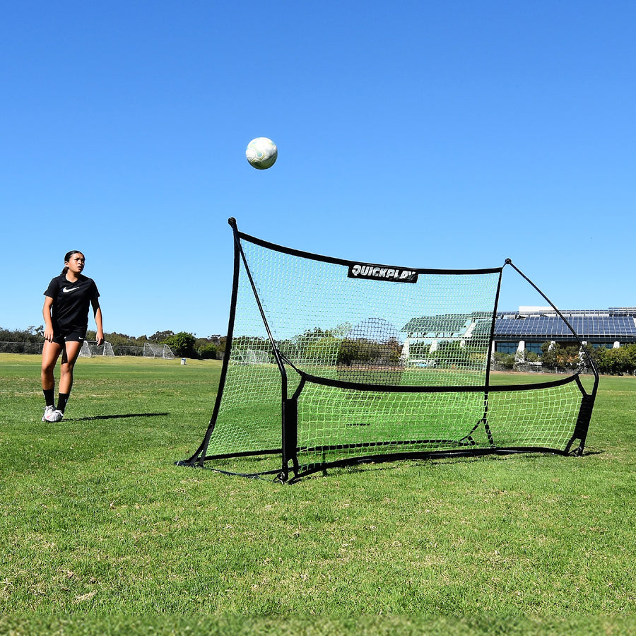 Joueur regardant un ballon s'élever depuis le filet du TEKKERS Trainer, vue de face du rebondisseur sur un terrain en herbe.