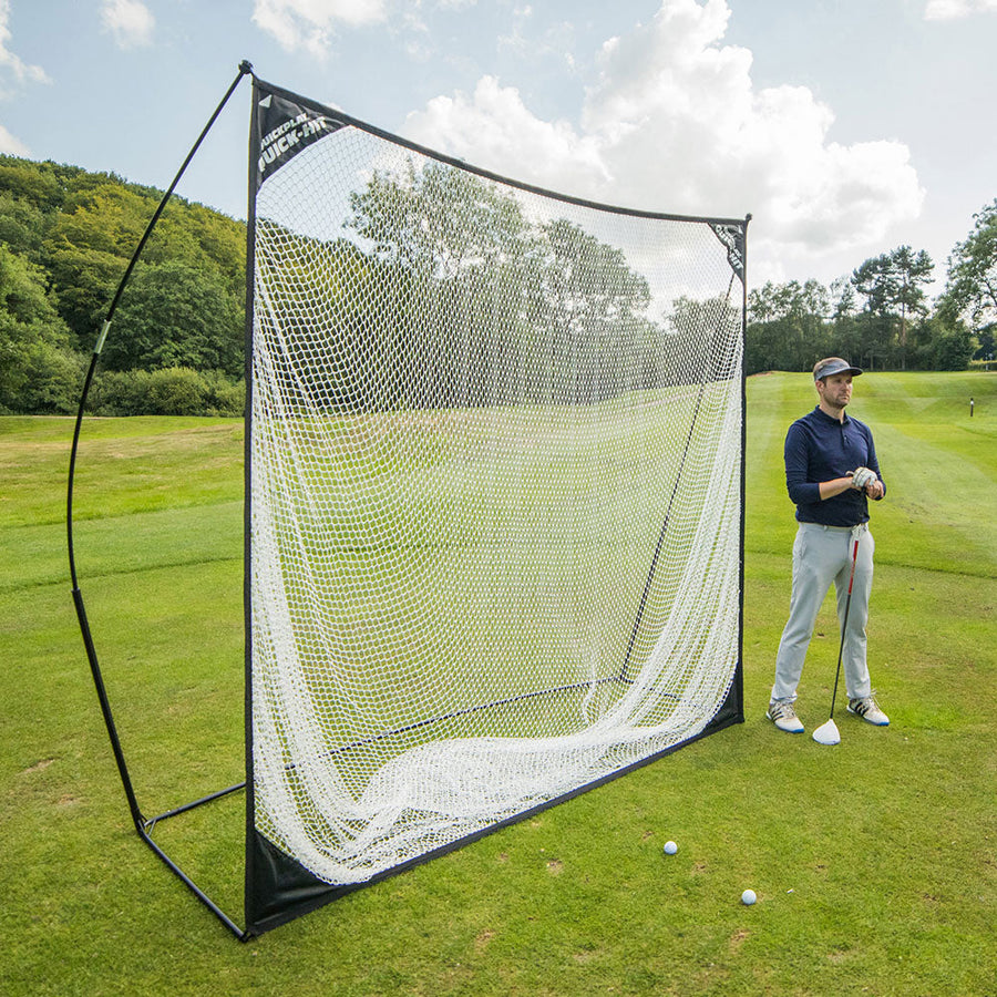 Filet de golf QUICK-HIT 240 x 240 cm installé sur un parcours de golf, avec un golfeur tenant un club à côté et des balles sur l'herbe.